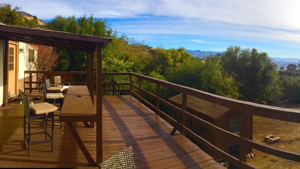 A wooden deck with outdoor furniture, a pergola, and a view of a mountainous landscape.