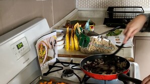 A kitchen with a stove, a tray of roasted sweet potatoes, and various food items on the counter.