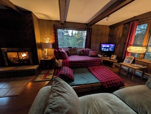 A cozy room with a fireplace, a bed with checkered bedding, a television, and a window with a view of trees. - Cozy, comfy, rustic ski chalet at the foot of Ski Brule ski mountain (Iron River)
