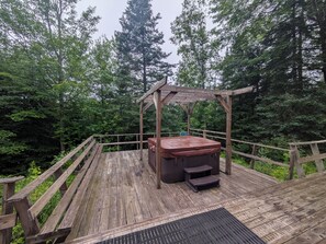 A wooden deck with a hot tub and a pergola, surrounded by dense forest. - Cozy, comfy, rustic ski chalet at the foot of Ski Brule ski mountain (Iron River)