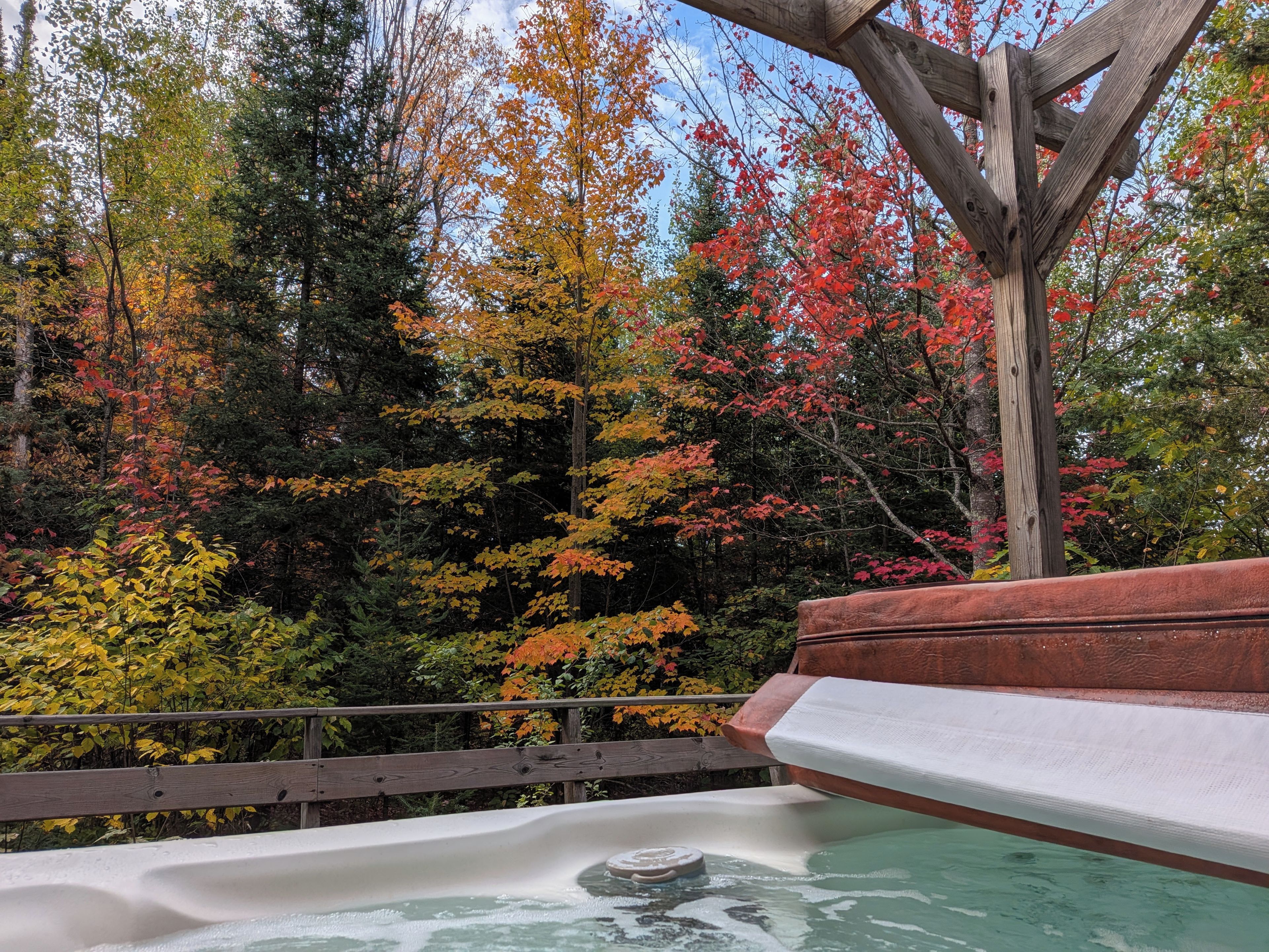 A hot tub with a wooden deck and a view of autumn trees.