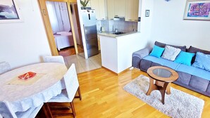 A compact living space with a dining area, a sofa with blue cushions, and a kitchen in the background. - Aquamarine beach apartment- terrace, seaside (Split)
