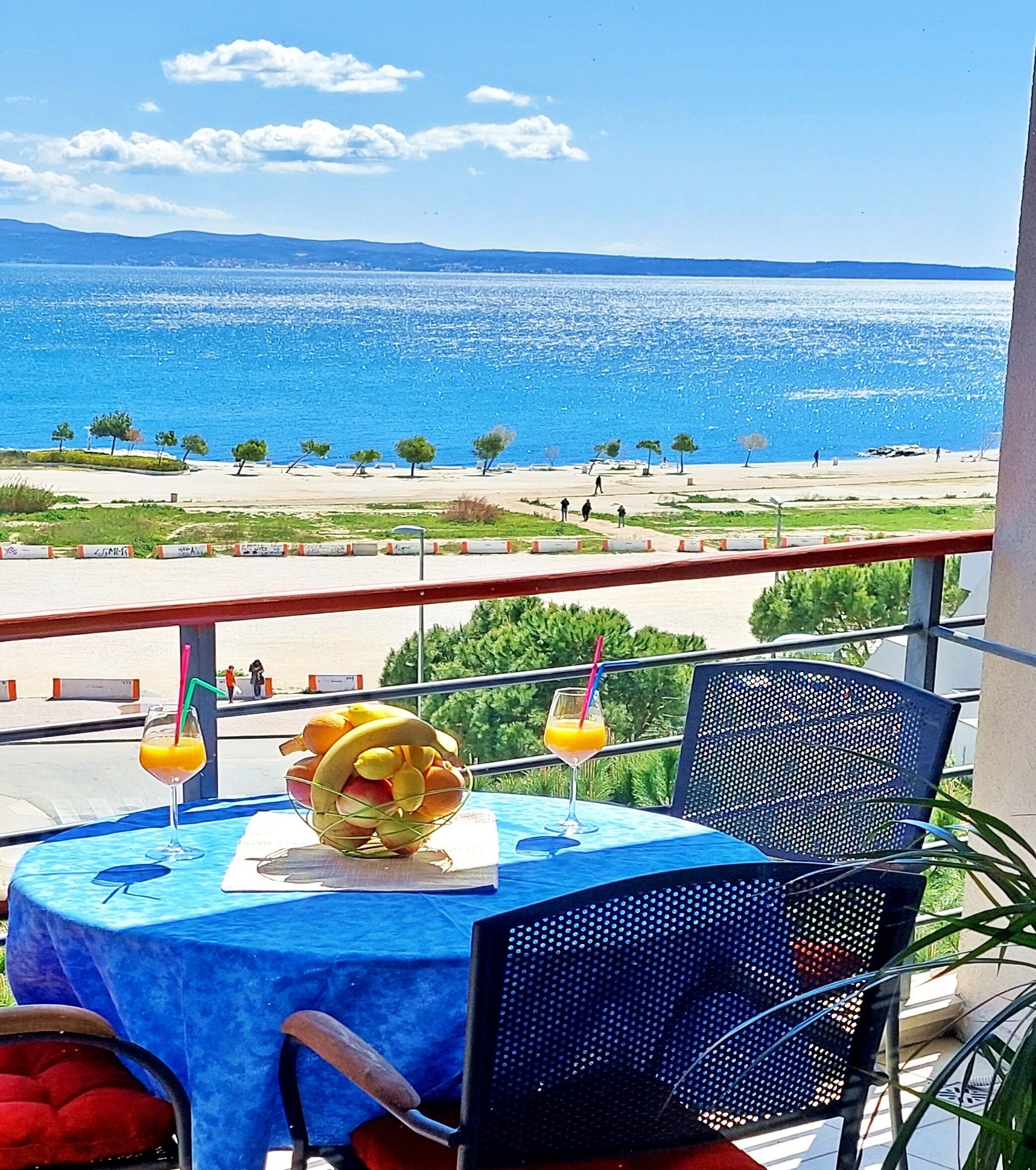 A balcony with a table set for two, overlooking a beach and the sea.