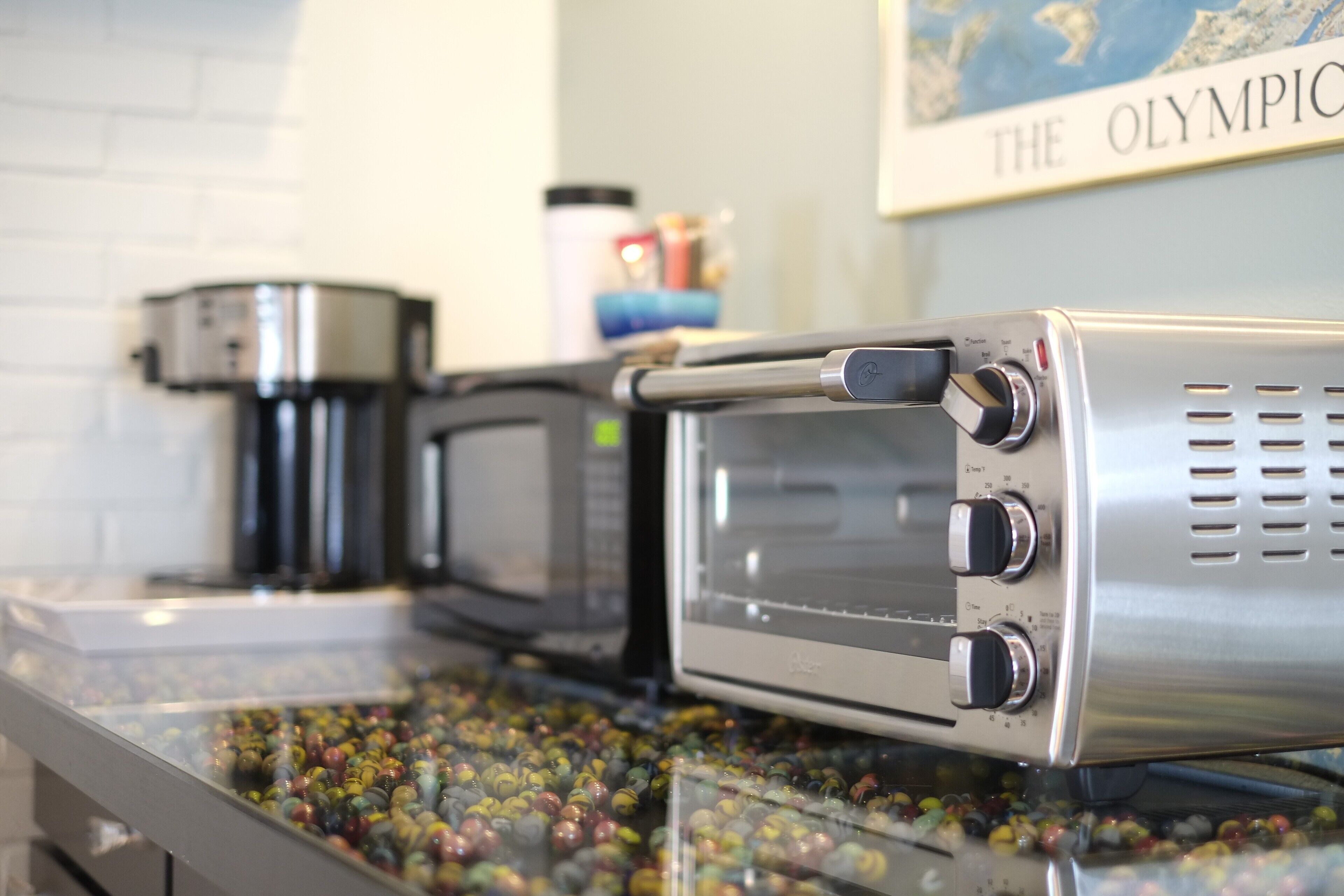 A coffee machine and a toaster oven on a counter with a glass container of colorful marbles.