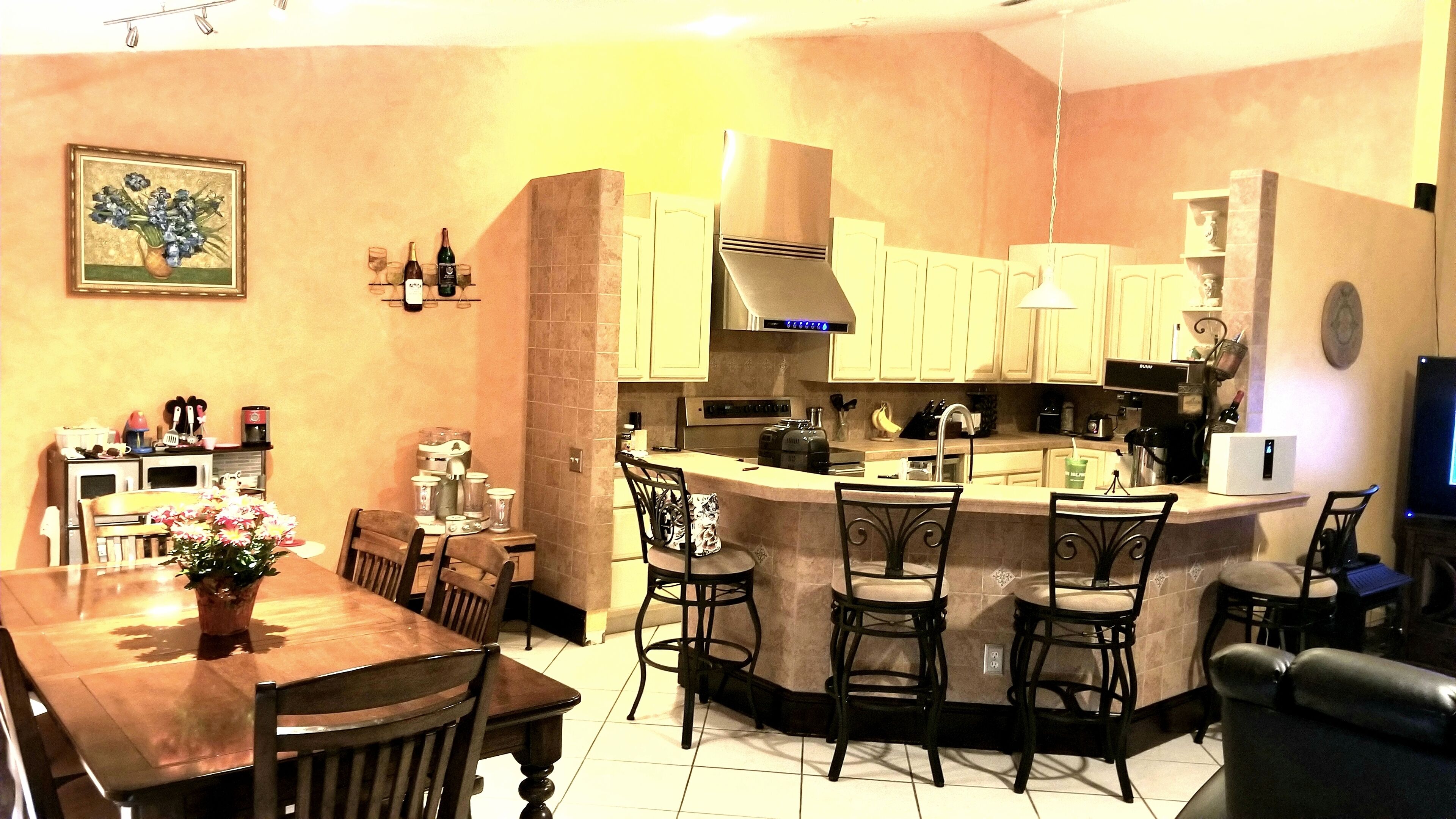 A kitchen with a central island, a dining area with a wooden table and chairs, and a small bar area with stools.
