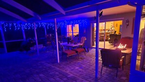 An outdoor patio area with brick flooring, covered seating, and a fire feature.