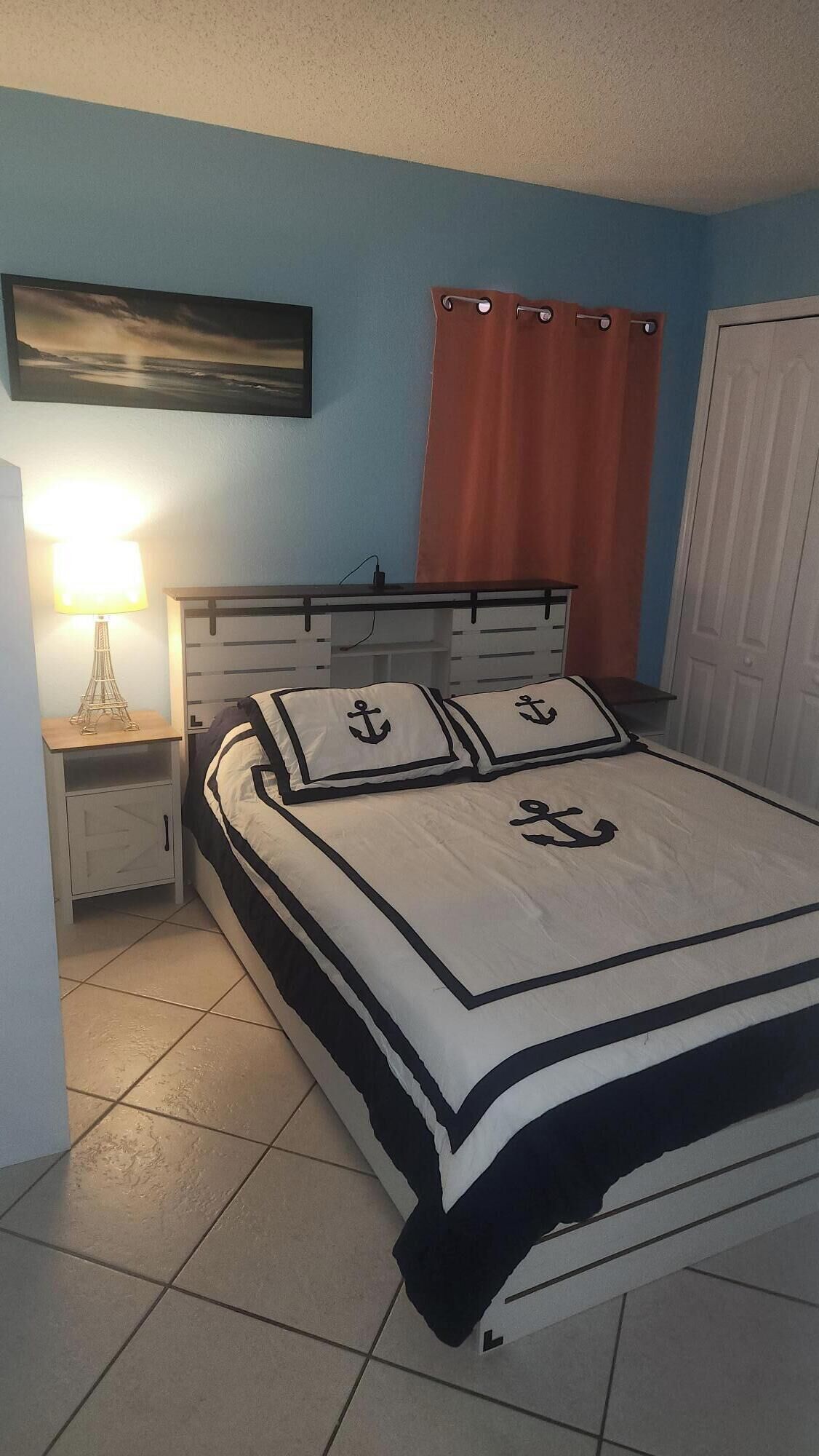 Une chambre à coucher avec un lit, une table de chevet, une lampe, un tableau et une porte.