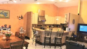 A kitchen with a central island, bar stools, a dining table with chairs, and a television on a stand.