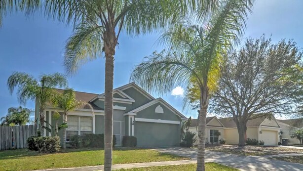 A residential house with a garage, surrounded by a wooden fence and palm trees.