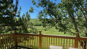 A wooden deck with a table and chairs, overlooking a green landscape with trees and hills. - A wonderful, secluded 2 story cabin, deck, fire pit, stocked pond for fishing.   (Paradise)