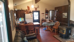 A cozy living room with a leather couch, wooden dining table, and chairs. A fireplace is visible in the corner. - A wonderful, secluded 2 story cabin, deck, fire pit, stocked pond for fishing.   (Paradise)