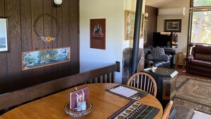 A cozy living room with a wooden wall, a fireplace, a leather sofa, and a dining area with a wooden table. - A wonderful, secluded 2 story cabin, deck, fire pit, stocked pond for fishing.   (Paradise)