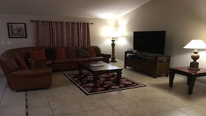 A living room with a brown leather sofa, a coffee table, a TV stand, and two lamps. - Beautiful Home near Walt Disney World   (Davenport)