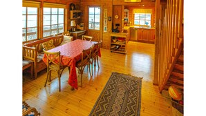 Una cabaña de madera espaciosa con comedor, cocina y una escalera que sube a un nivel superior.