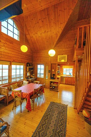 Una cabaña de madera espaciosa con comedor, cocina y una escalera que sube a un nivel superior.
