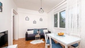 A modern living room with a sofa, a dining table with chairs, a television, and a window with curtains. - "City and Sea" apt in center, 5 min walk to the Diocletian’s palace and beach  (Split)
