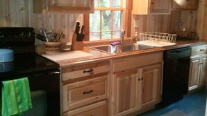 Una cocina con armarios de madera, un fregadero, una estufa y una ventana con vistas a árboles.