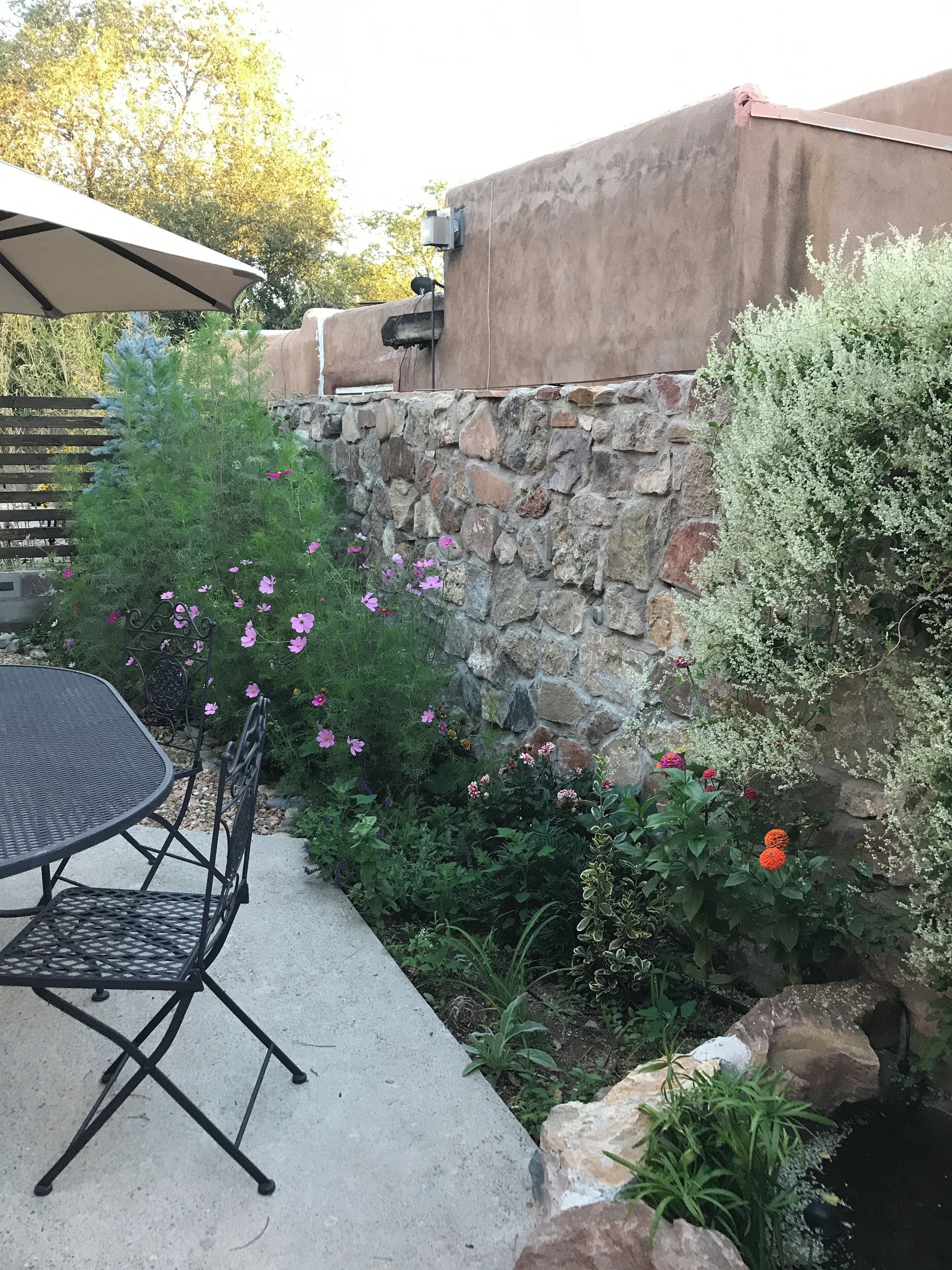 A patio with a table and chairs, surrounded by a stone wall and various plants.