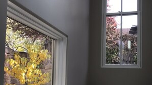 A bedroom with a bed, two pillows, a window with a view of a tree with yellow leaves, and a stone wall. - Feel at Home , all sanitized, 6 walkable blocks from Santa Fe Plaza. (Santa Fe)