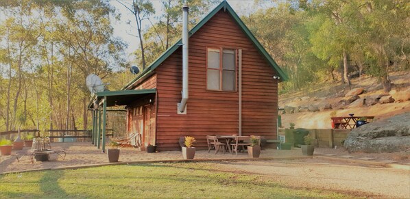 A wooden cabin with a pitched roof, a satellite dish, and a small patio with outdoor furniture.