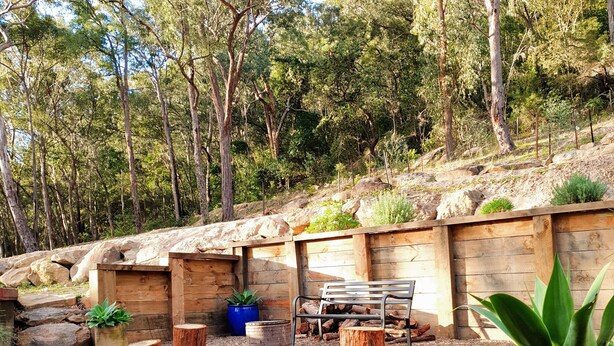 Eine Holzterrasse mit einer Bank, umgeben von Topfpflanzen und einer rustikalen Holzwand.
