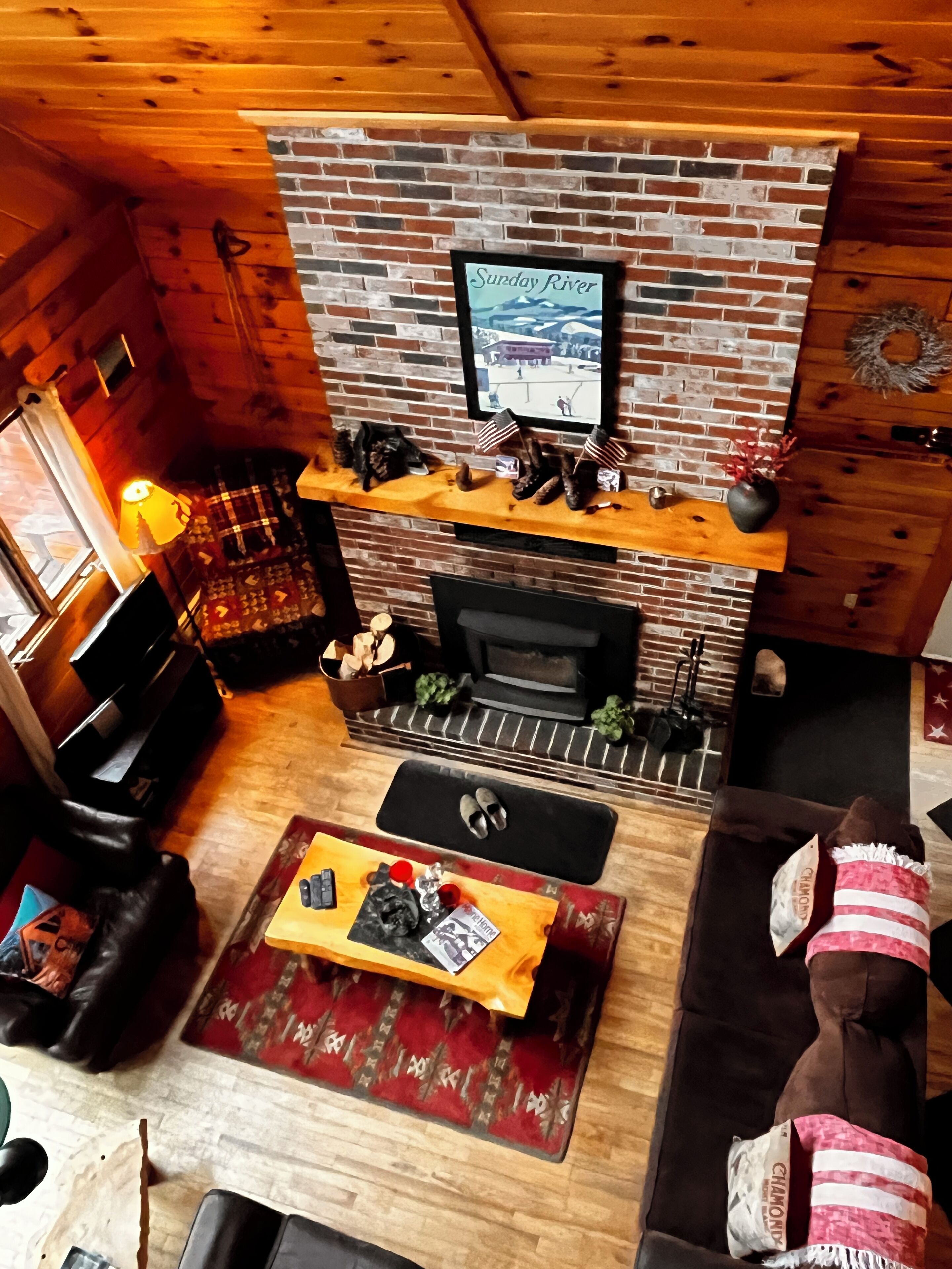 A cozy living room with a brick fireplace, a television mounted above it, and a wooden ceiling.