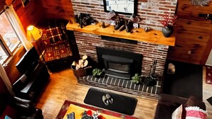 Una sala de estar acogedora con una chimenea de ladrillo, un televisor montado encima y un techo de madera.