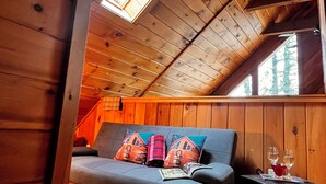 Interior acogedor de una cabaña con techo de madera, un sofá con cojines coloridos, una mesita con vasos y una planta en maceta.