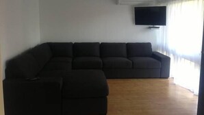 A living room with a sectional sofa, a flat-screen TV mounted on the wall, and a ceiling fan. - Beach Break - located at Kiama (Kiama)