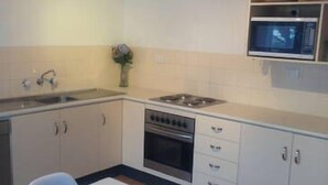 A kitchen with white cabinets, a microwave, a stove, and a sink. - Beach Break - located at Kiama (Kiama)