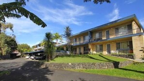 A two-story building with a stone retaining wall and a grassy lawn. - Beach Break - located at Kiama (Kiama)