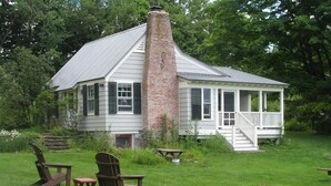Uma casa com chaminé de tijolos, varanda e gramado com duas cadeiras Adirondack.