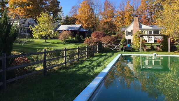 Um jardim tranquilo com piscina, cerca de madeira e casas ao fundo.