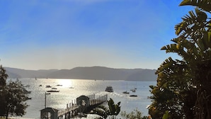 Un paysage côtier avec des bateaux sur l’eau, une jetée et des montagnes en arrière-plan.