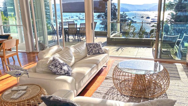 Un salon moderne avec un canapé en cuir blanc, une table basse ronde en osier et une vue sur une marina remplie de bateaux.