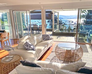 A modern living room with a white leather sofa, a round wicker coffee table, and a view of a marina with boats. - #1 Location at Palm Beach (Palm Beach)