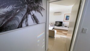 Un couloir mène à une chambre où se trouvent un lit, un téléviseur et un tableau accroché au mur.