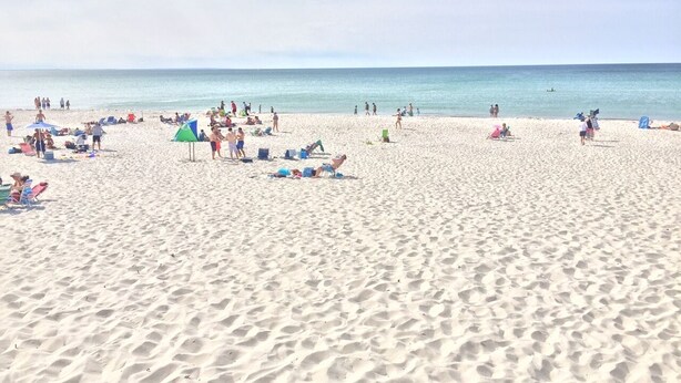 Ein Sandstrand mit Menschen und Sonnenschirmen.