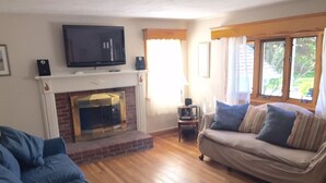 Ein Wohnzimmer mit Kamin, Fernseher, einer Couch und einem Fenster mit Vorhängen.