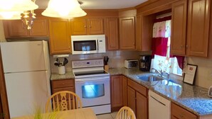 Eine kleine Küche mit Holzausbau, einem weißen Kühlschrank, einer Mikrowelle, einem Backofen, einem Spülbecken und einem Esstisch mit Stühlen.