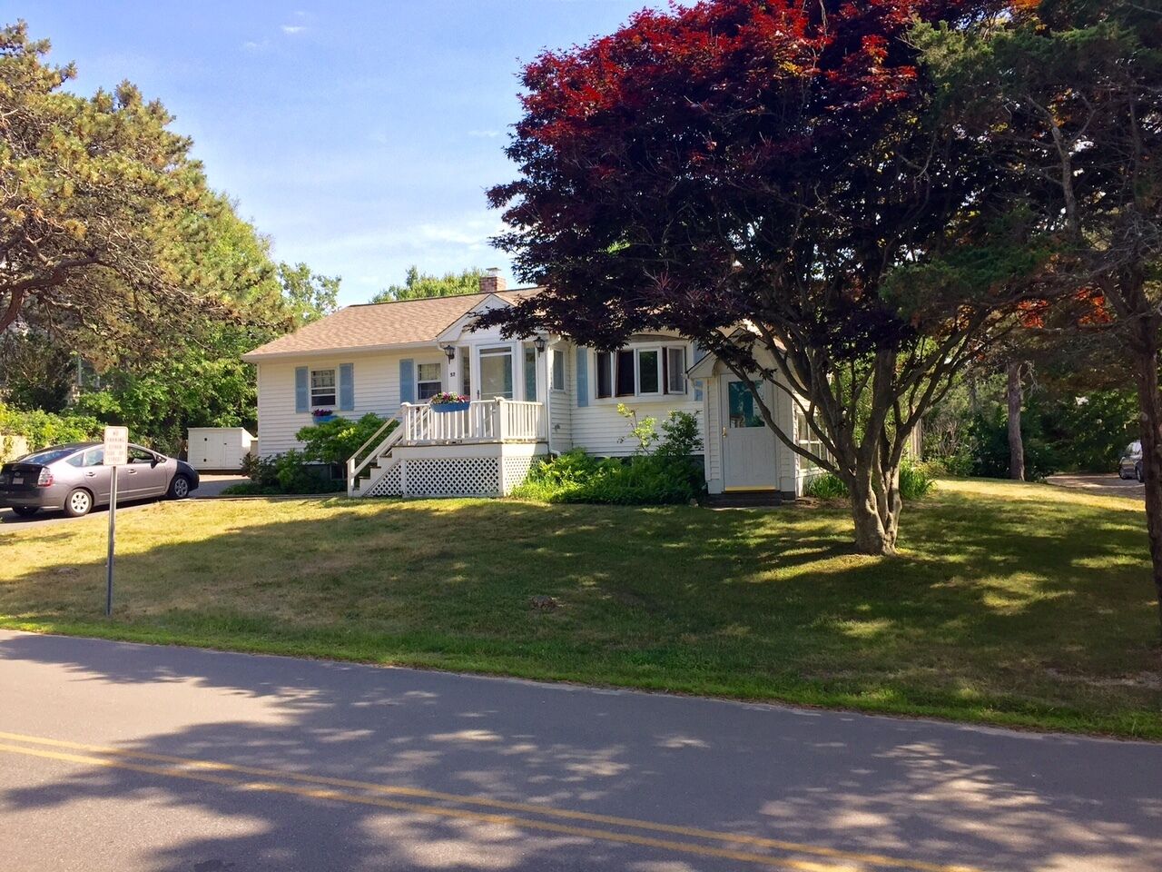 A single-story house with a front porch, a driveway, and a tree with autumn leaves.