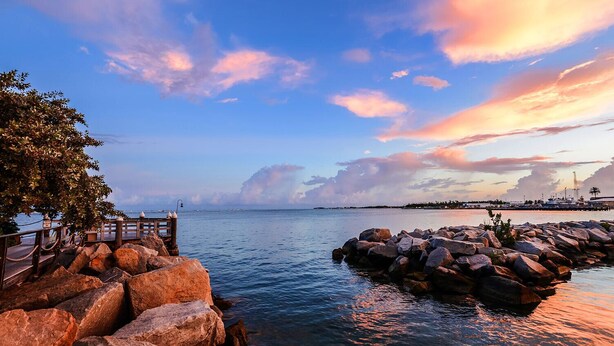 A coastal scene with a wooden pier, rocky breakwaters, and a clear view of the sea. - Galleon Resort Efficiency in the old town (Key West)