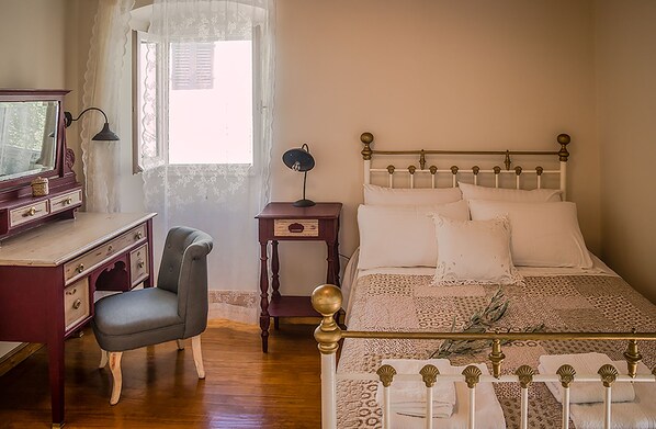 A bedroom with a wooden desk, a chair, a bed with white linens, and a window with lace curtains.