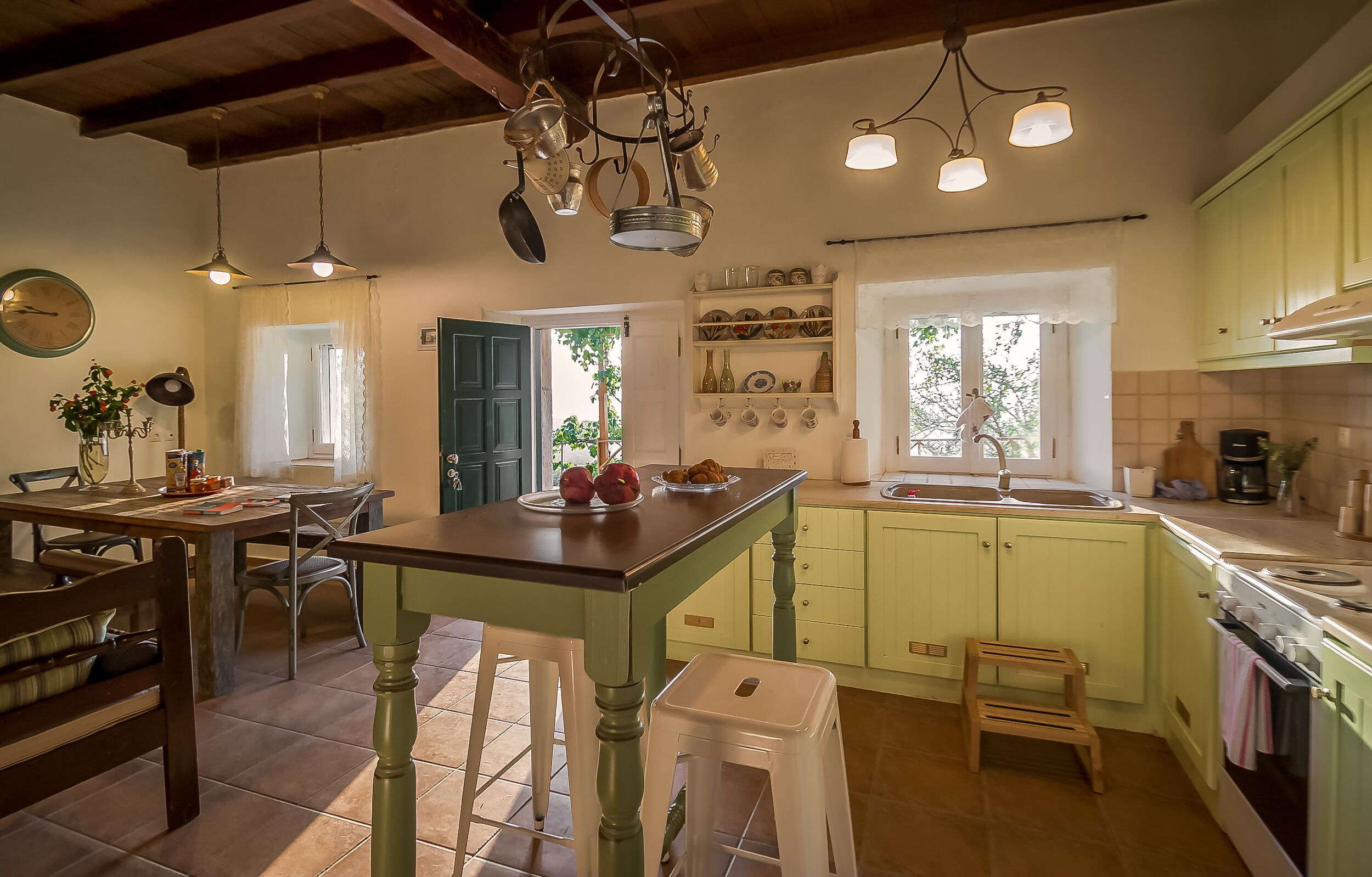 A kitchen with a wooden table, stools, and a hanging pot rack.