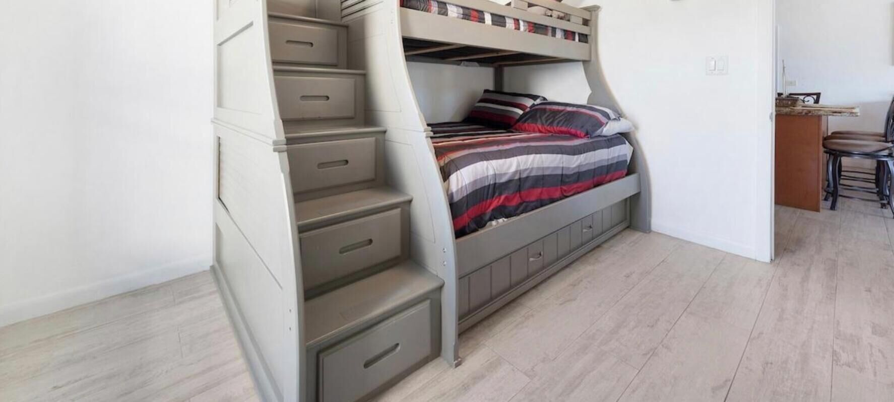 A bunk bed with storage drawers, a desk, and a chair in a room with light wooden flooring.