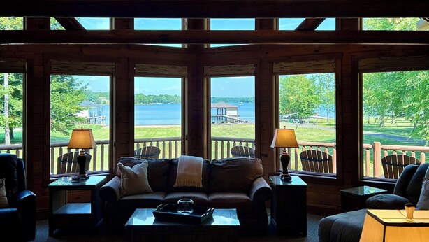 A spacious room with a high ceiling, large windows, and a view of a lake.