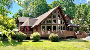 A log cabin with a large deck, multiple windows, and a well-maintained lawn.