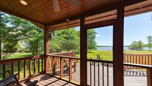 A wooden deck with a view of a lake and grassy area.