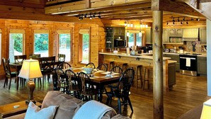 A spacious log cabin interior with a dining area, kitchen, and a loft bedroom.