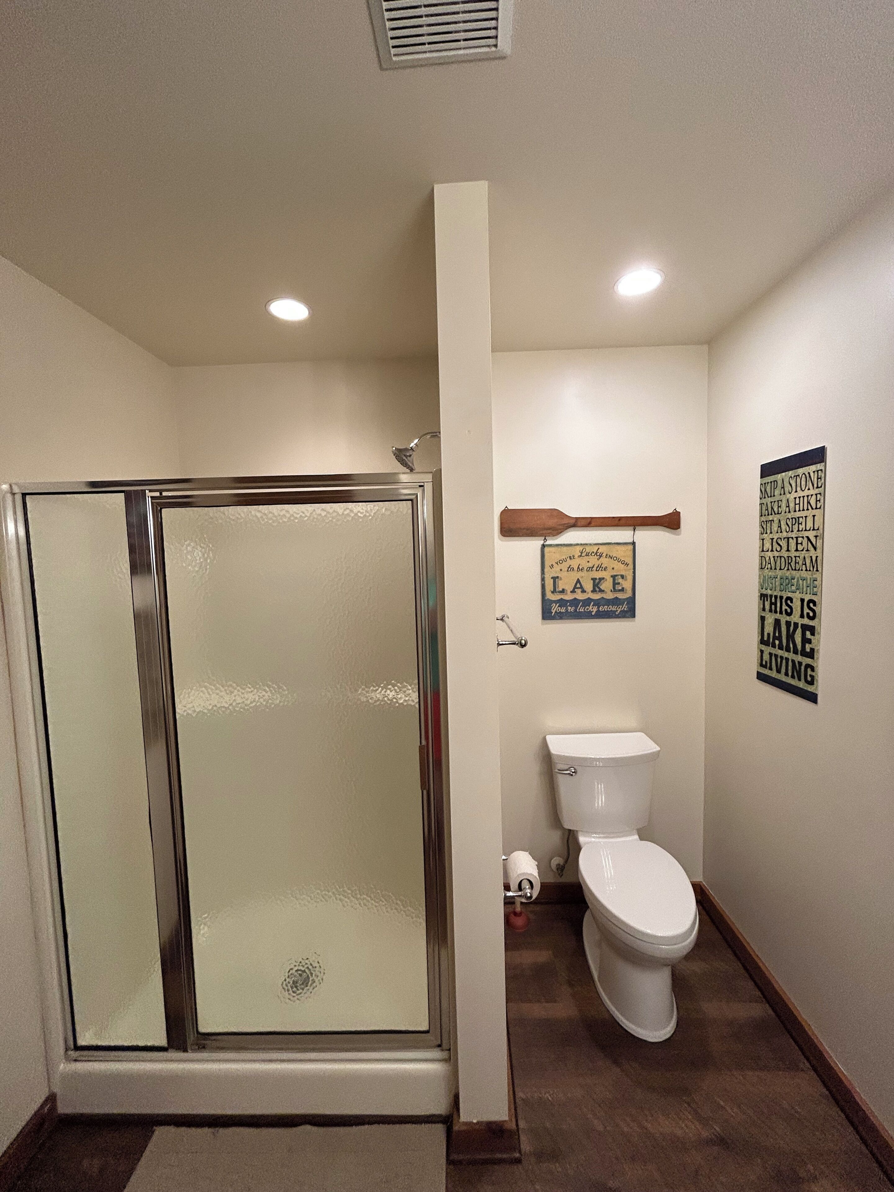 A bathroom with a glass shower enclosure, a toilet, and a wall-mounted wooden bathtowel rack.